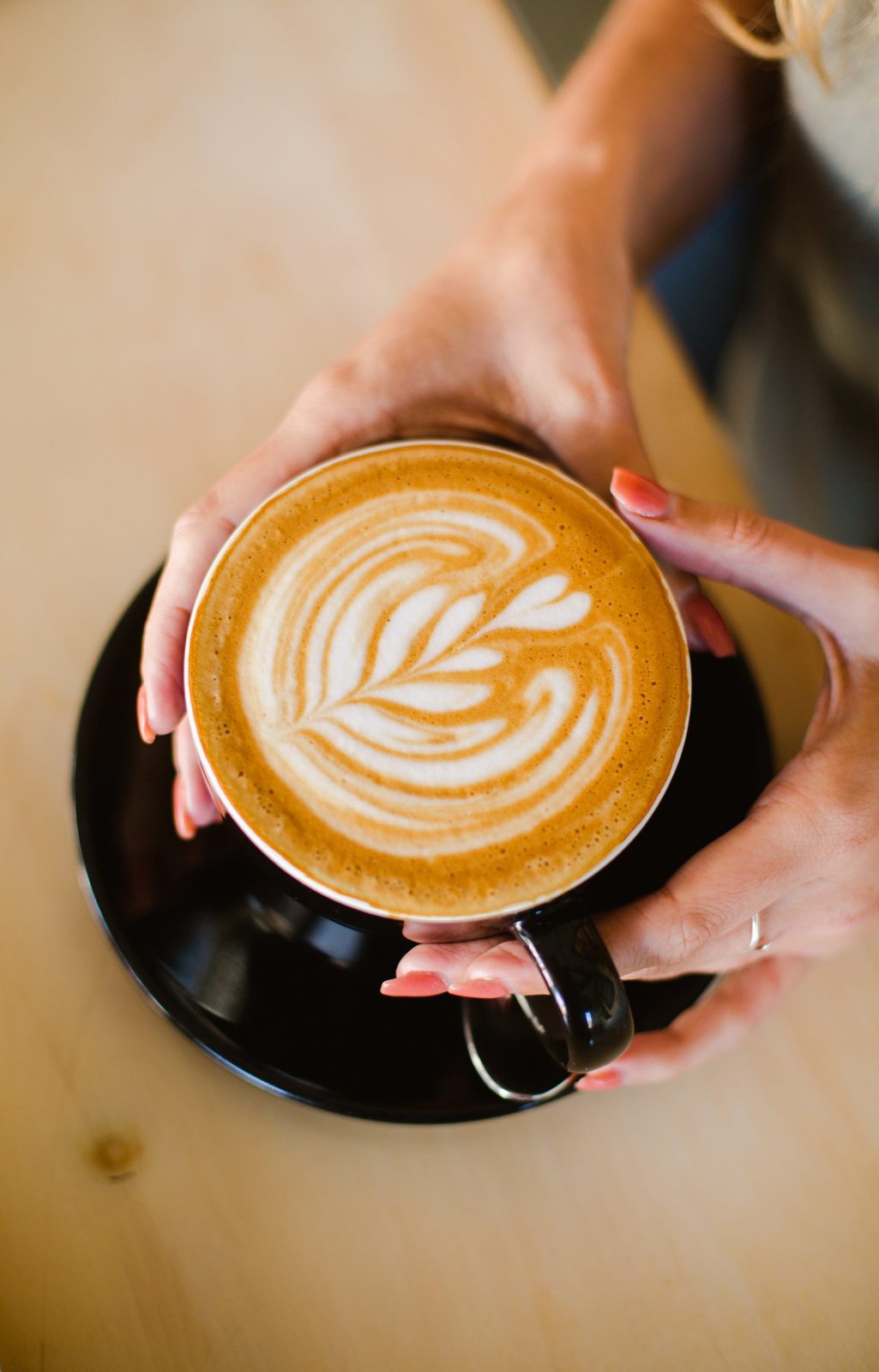 Handen om een kop cappuccino met latte art